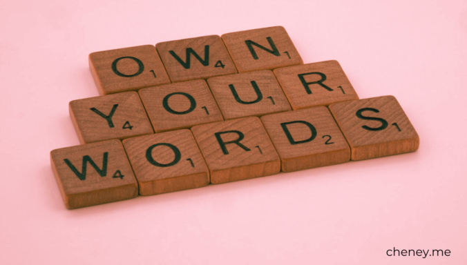 "Own your words" spelled out in scrabble tiles on a pink background